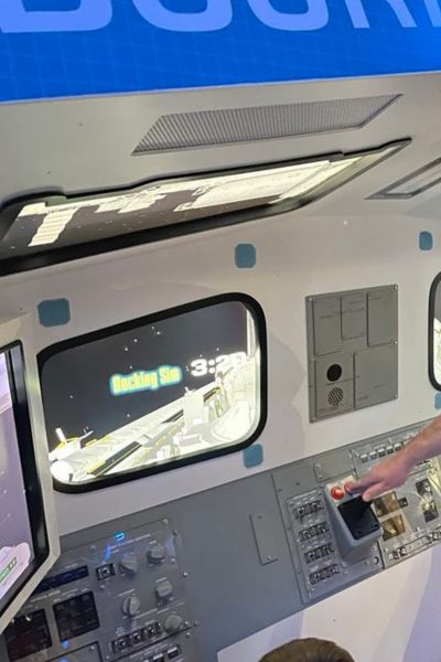 A close-up of a space simulation cockpit with screens showing a docking mission.