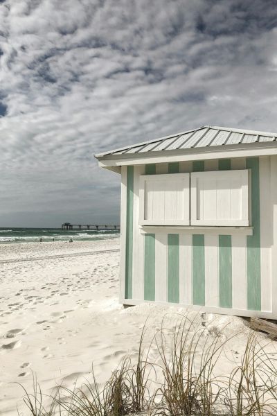 A small beach hut with green and white stripes stands on soft white sand.