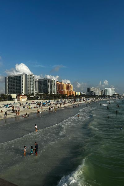 People enjoying the sunny beach with city buildings in the background.