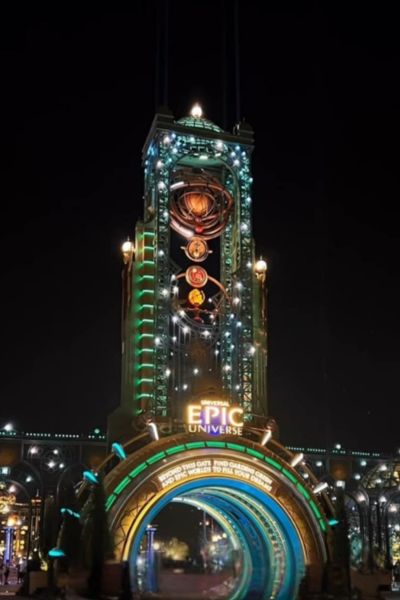 Brightly lit Universal Epic Universe entrance at night with colorful lights and glowing signs.