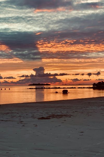 A calm beach at sunset with orange and purple clouds reflecting on the water.
