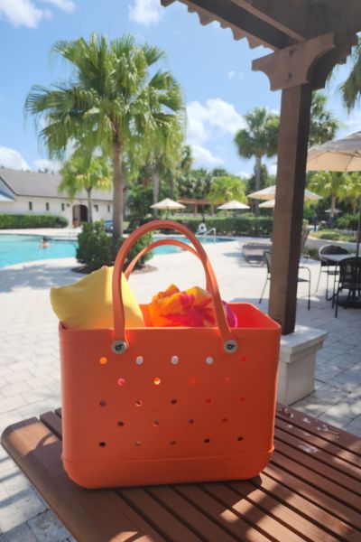 Orange tote bag holding beach towels by the pool and palm trees.