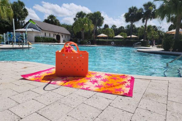 Sunny day by the pool with a palm tree pattern towel and orange tote.