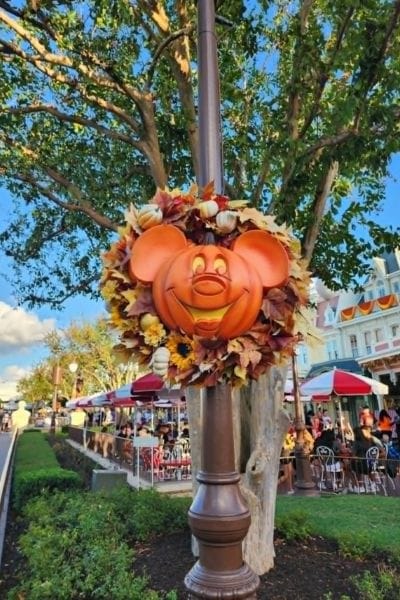 Mickey pumpkin wreath hanging from a lamppost at Magic Kingdom with fall leaves and Halloween decorations for Mickey’s Not-So-Scary Halloween Party.