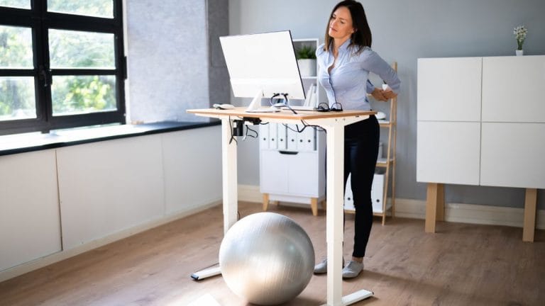 Woman using a standing desk in a bright home office with an exercise ball, featuring some of the best work from home productivity tools for a comfortable workspace.