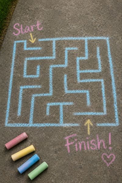 Colorful sidewalk chalk sticks lined up on pavement with bright chalk lines, featuring creative sidewalk chalk drawing ideas for screen free summer fun with kids.