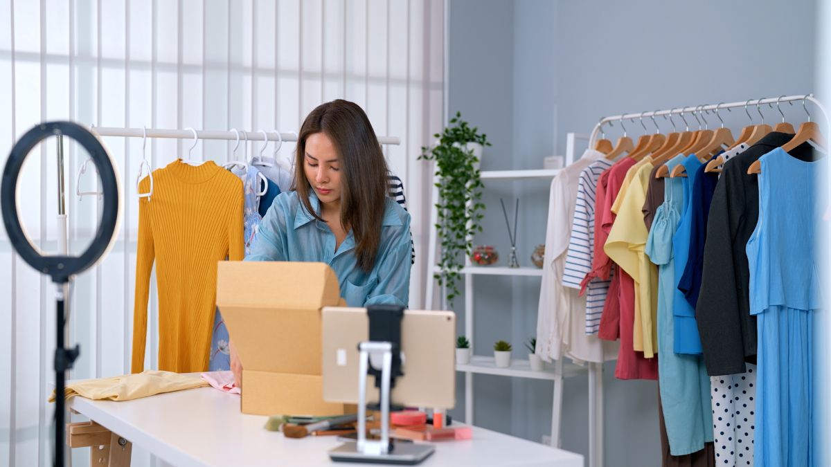 Woman preparing clothing inventory for a live selling show, with a ring light, tablet, boxes, and colorful clothes, representing common Whatnot seller mistakes beginners should avoid.