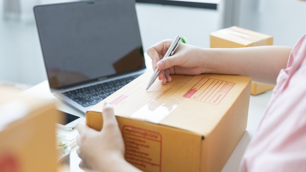 Person packing a shipping box with a laptop nearby, showing whatnot seller supplies for preparing and shipping live sale orders.